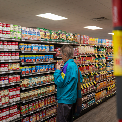 A woman studies an aisle of canned goods in a grocery store.