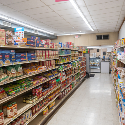 A photo looking down the middle of a grocery store aisle. Colorful boxes of noodles and jars of sauce are on one side with bags of flour, colorful boxes of jello and cans of pie filling are on the other side.