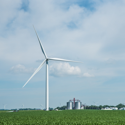 Wind turbine in a farm field with crops surrounding it and farm operation in the background.