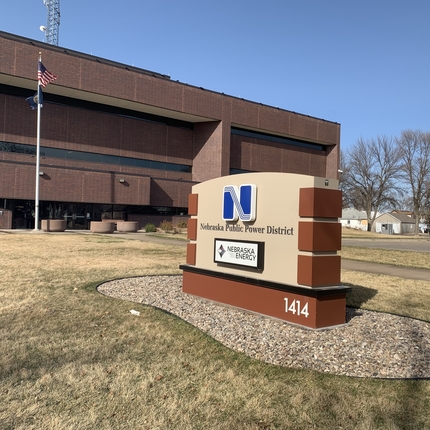 Un letrero que decía Distrito de Energía Pública de Nebraska con un edificio de oficinas al fondo.
