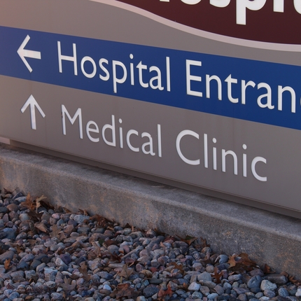Letrero gris con entrada al hospital en blanco sobre fondo azul y Clínica médica en texto blanco sobre fondo gris.