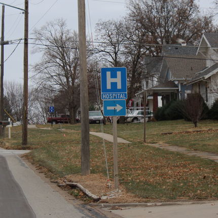 A blue street sign that says "H" with the word "HOSPITAL" and a right-pointing arrow beneath it.