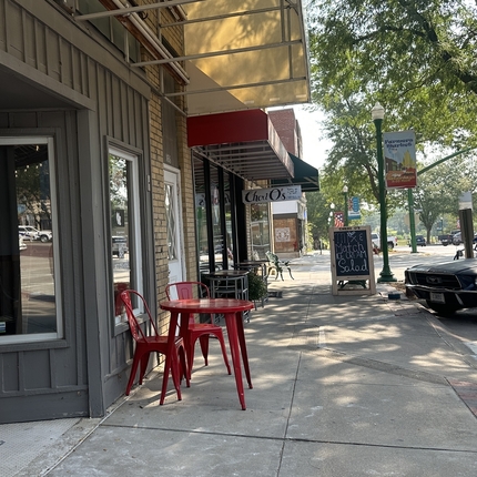 red table and chairs sitting outside main street buildings with a black car parked on the street.