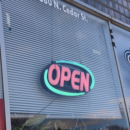 Electric open sign hangs from window in front of white blinds