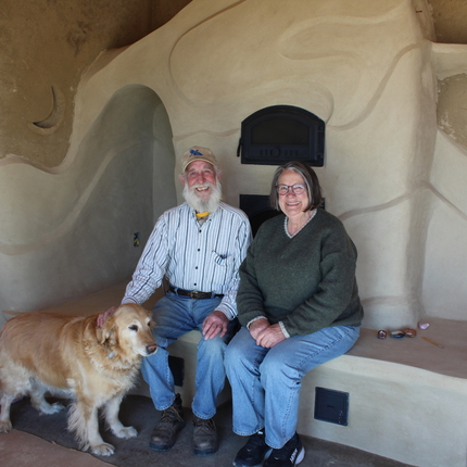 Hombre y mujer sentados en una chimenea de arcilla con un perro dorado parado frente a ellos