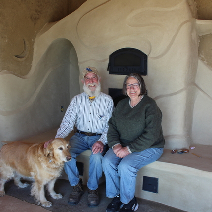 Man and woman sitting on a clay fireplace with a golden dog standing in front of them