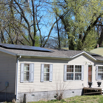 Casa de un piso de color blanquecino con dos paneles solares en el techo