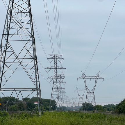 Altas torres de transmisión de metal con líneas eléctricas que se extienden en la distancia a través de un campo verde bajo un cielo nublado.
