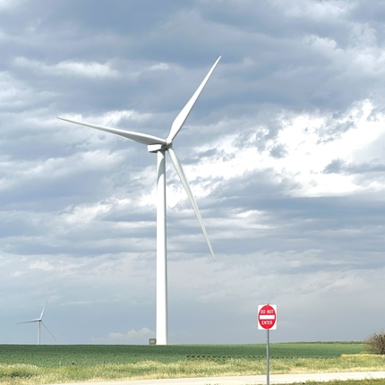 Turbina eólica de color blanco sentada en un campo rural junto a una carretera