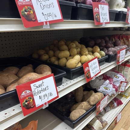 Grocery store shelves filed with potatoes and onions.
