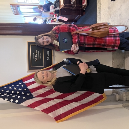 Dues dones davant d'una pancarta a l'exterior d'una oficina que diu "Deb Fischer Nebraska" i una bandera americana.