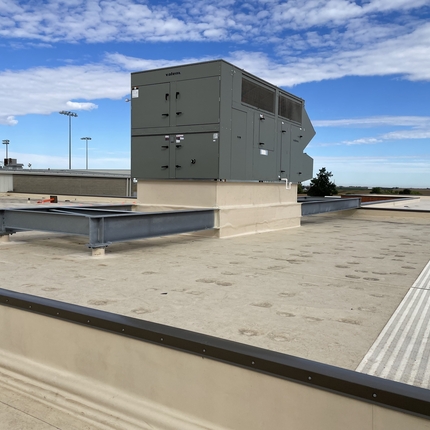 Aire acondicionado y calefacción en la azotea de un edificio con tejado plano. Cielo azul con nubes tenues al fondo.