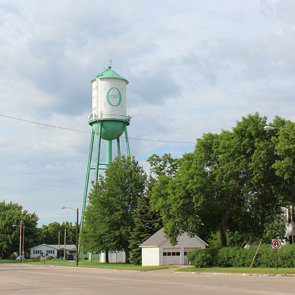 Water tower that's white with a green top and green bottom, on a street with mature trees and houses