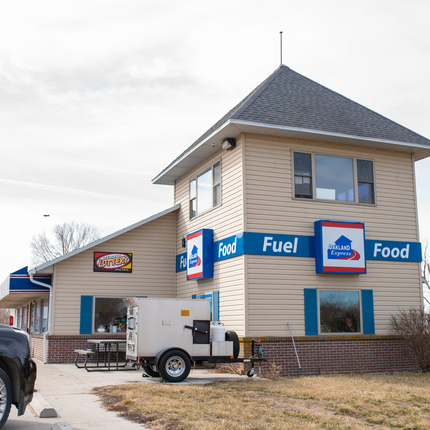 Large two story building with fuel and food wording on the side on blue sign, part of a black suv is parked in the left bottom corner of the image