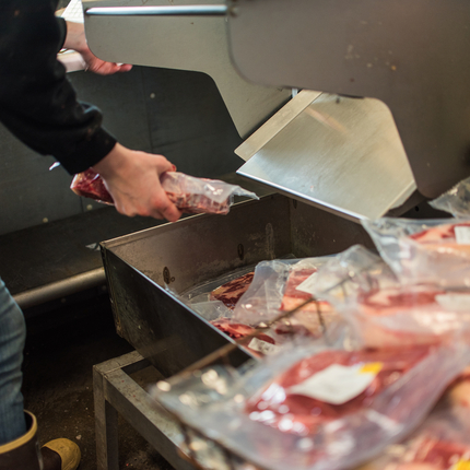 a person picking up a package of meat from a machine, with packages of meat on a table nearby