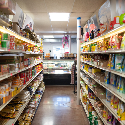 Pasillo en una tienda de comestibles de propiedad local con estantes de productos alimenticios a ambos lados del pasillo y un mostrador de carne en el frente.
