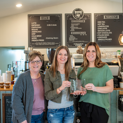 Tres mujeres blancas en una cafetería se toman una foto con un premio en mano