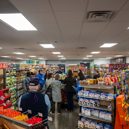 Several people stand in a small, rural grocery store conversing in between aisles. 