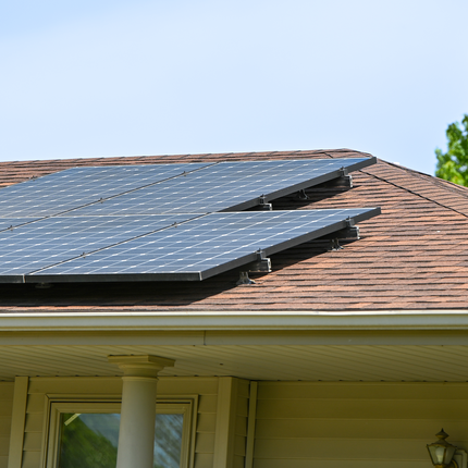 Rooftop solar panels installed on a house with brown asphalt shingles, capturing sunlight under a clear blue sky.