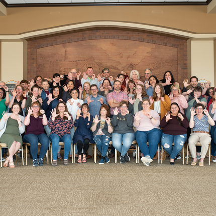 Large group of people, mostly white and Latino, in four rows holding up 5 + 0 for 50 years