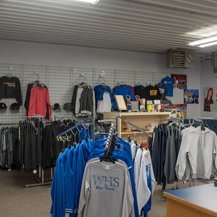 A variety of long sleeve clothing apparel in different colors hang on racks and on the wall inside a building