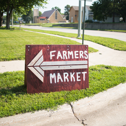 Letrero de jardín que dice mercado de agricultores con una flecha grande