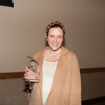 Woman in tan sweater holding a glass award