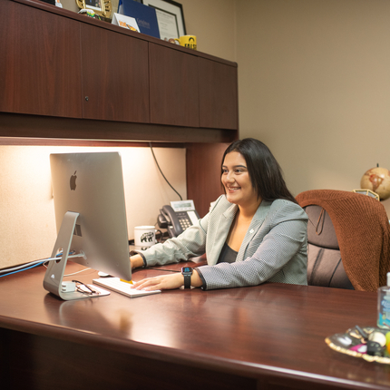 Mujer latina sentada en un escritorio en frene de una computadora IMac