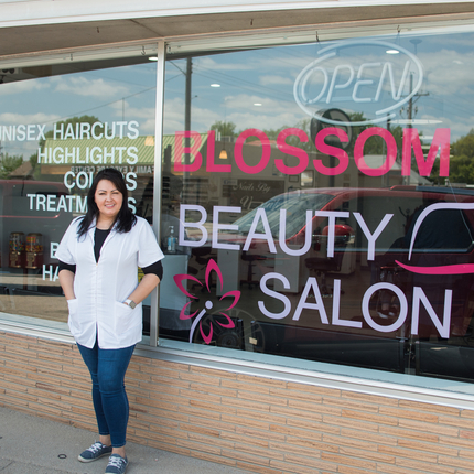 A woman standing in front of the outside of a business, with a sign that says "Blossom Beauty Salon"