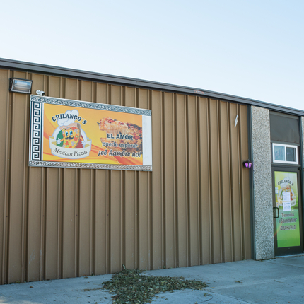 A brown building with a restaurant sign in front in yellow and orange color and a door to the far right of the building