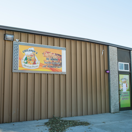El edificio de un negocio de color cafe con un anuncio en frente en color amarillo y naranja y una puerta hacia la derecha del edificio