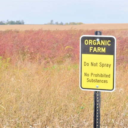 Organic Farm, do not spray sign with farm field in the background. 