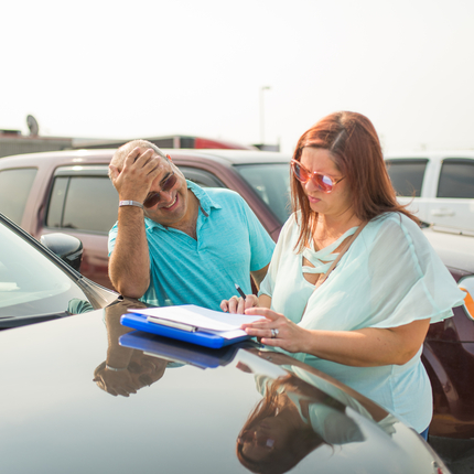 Man and woman filling out paperwork on the hood of a vehicle