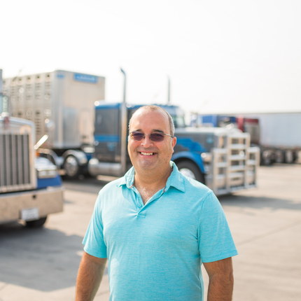 Man standing in front of two blue semis in parking lot