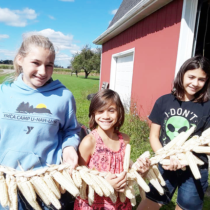 Three girls holding a string of corn with stalks braided