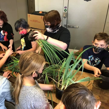 children in masks putting plants into pots