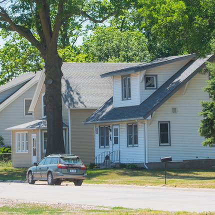 Small town street lined with three houses. Green vehicle parked on the side of the street.