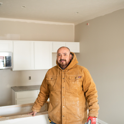 Man in thick brown jacket stands in front of a kitchen remodel