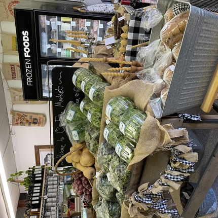 A vegetable stand inside a store, with several vegetable greens, squash, packaged bread in aluminum bin