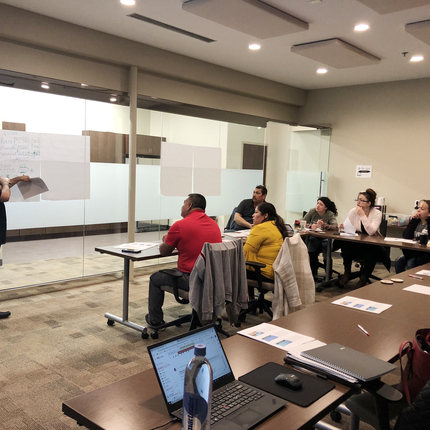 man teaching people sitting at tables, listening