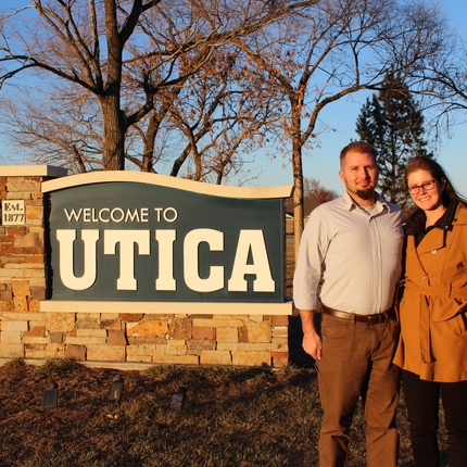 Man and Woman in front of town sign for "Utica"