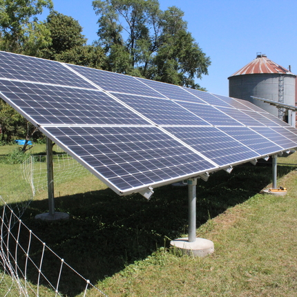 Solar panel with wire fencing around it, house and grain bin in background
