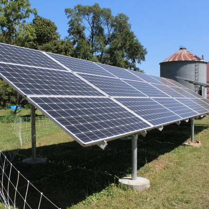 Solar panel with wire fencing around it, house and grain bin in background