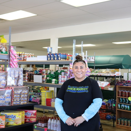 Woman stands in grocery store with racks of goods behind her