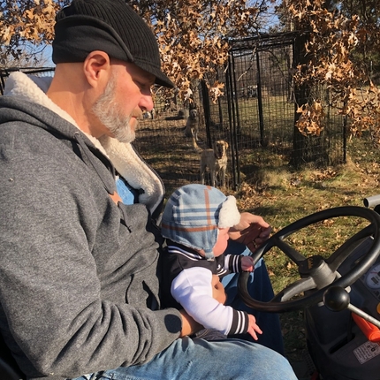 Man rides farm equipment with toddler on his lap