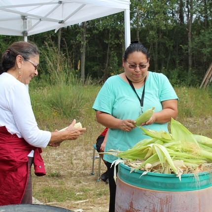 two women shucking corn, standing up