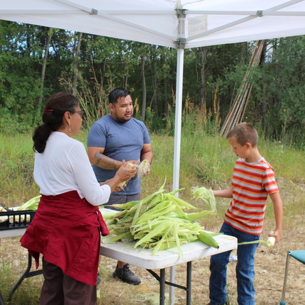 man, woman, and boy standing around table with corn shucks on them