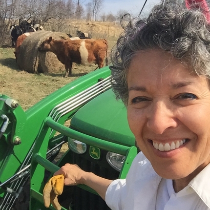 Woman on tractor smiles while cattle feed on hay in background