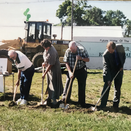three men and a woman shoveling dirt at a groundbreaking ceremony
