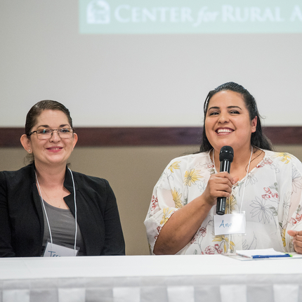 Dos mujeres sentadas a una mesa, una de ellas hablando por un micrófono.